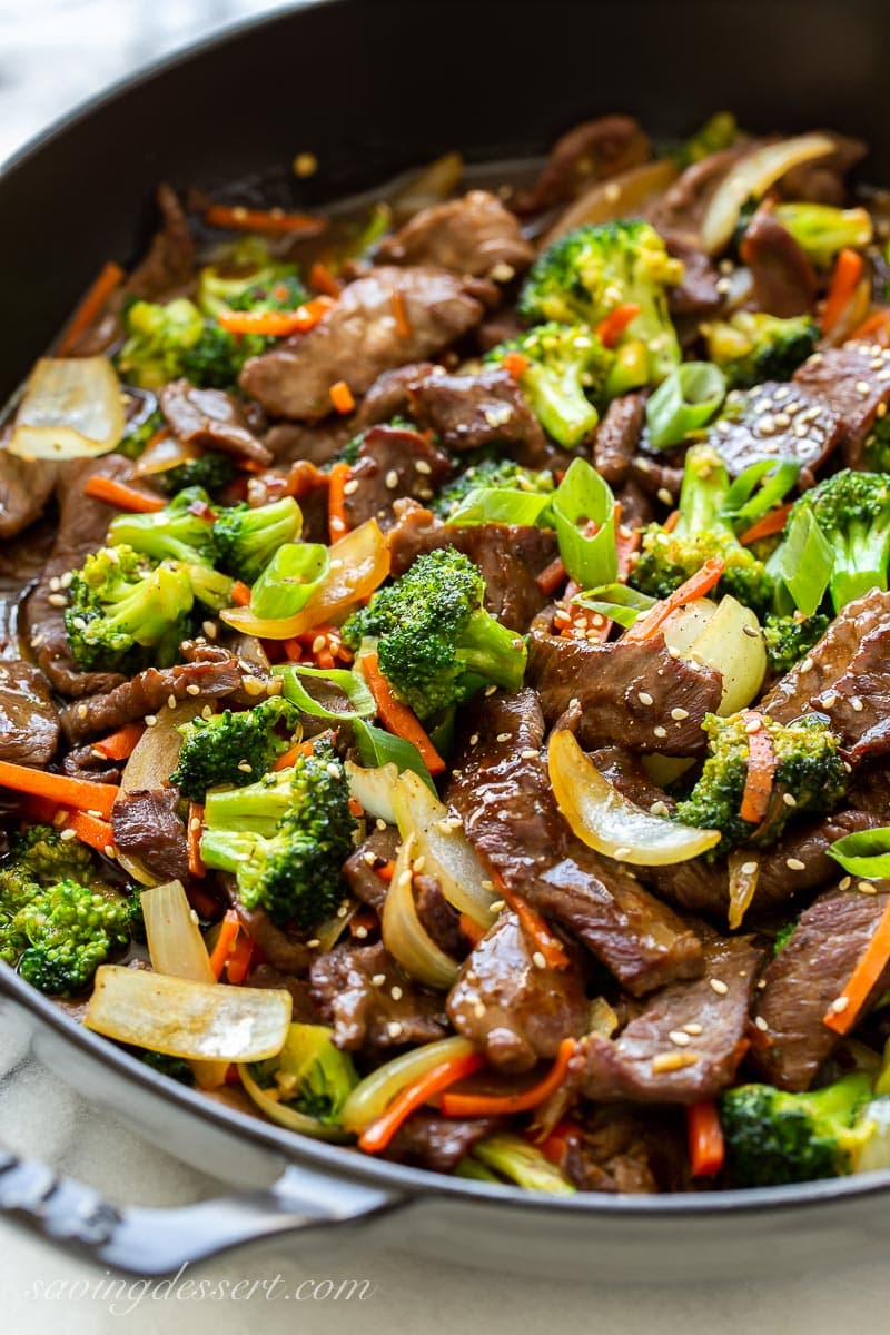 A skillet filled with thin sliced beef, broccoli, carrots and onions topped with sesame seeds