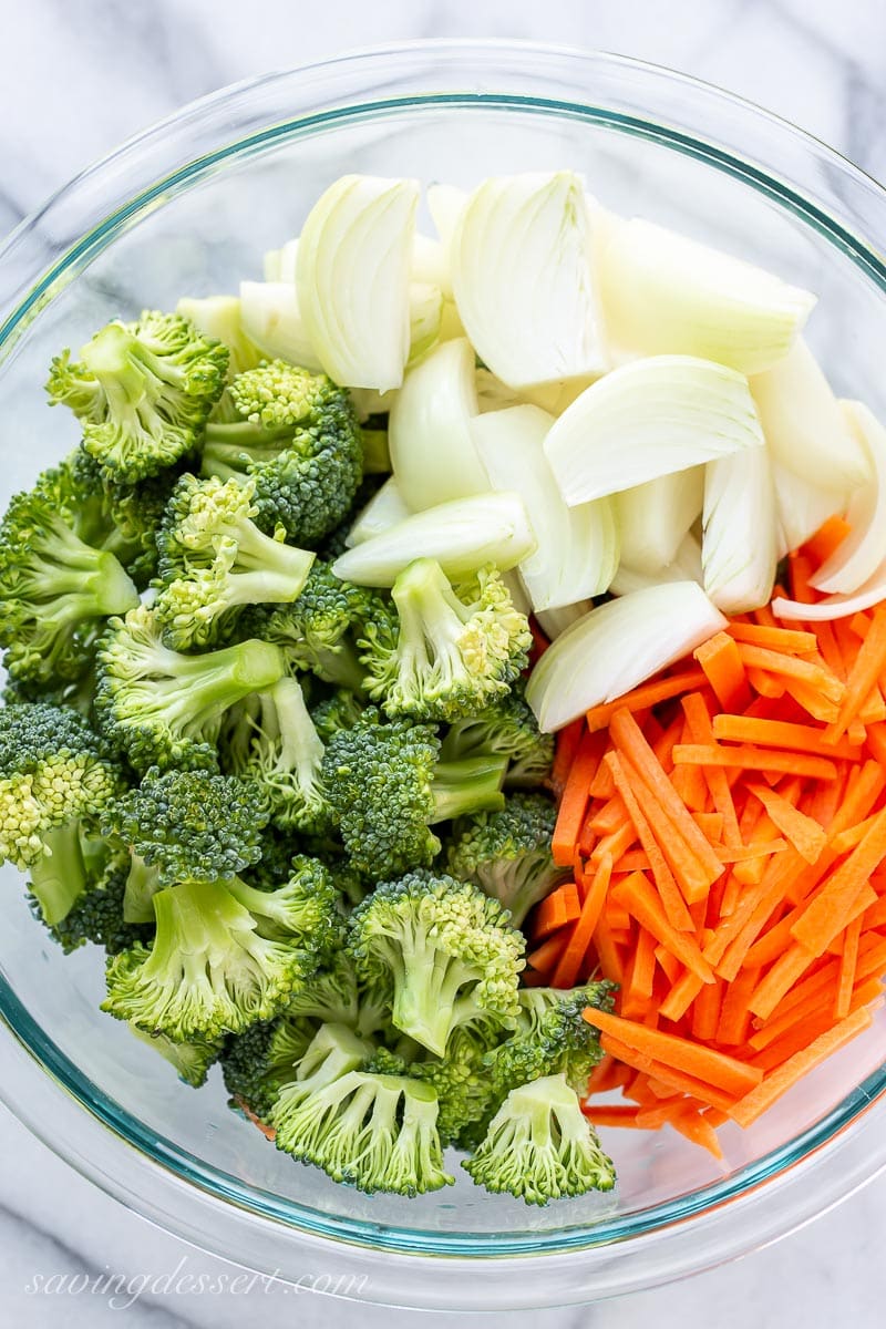 A bowl of raw broccoli, onions and carrot cut into matchsticks