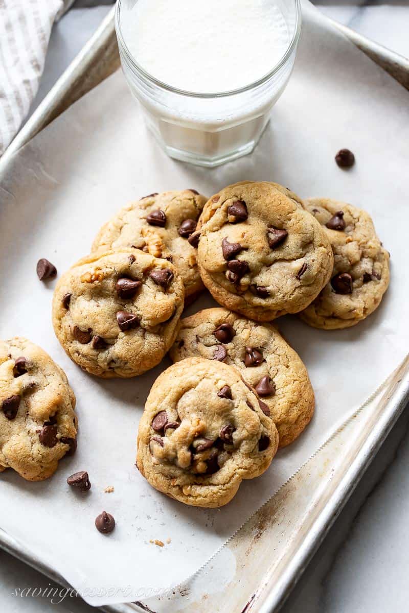 A small baking tray lined with parchment paper with a few cookies and a glass of milk