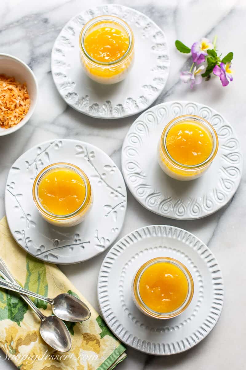 Four jars of coconut tapioca pudding topped with lemon curd on small plates.