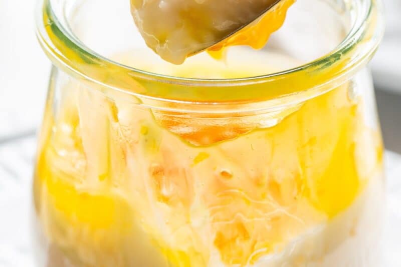A jar of tapioca pudding with lemon curd being scooped out with a spoon.