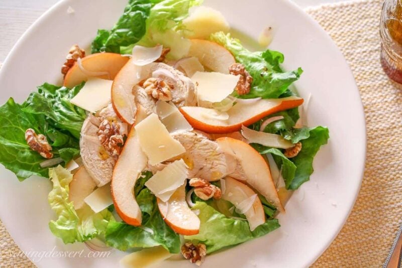 A plate with sliced chicken, pear and walnut salad