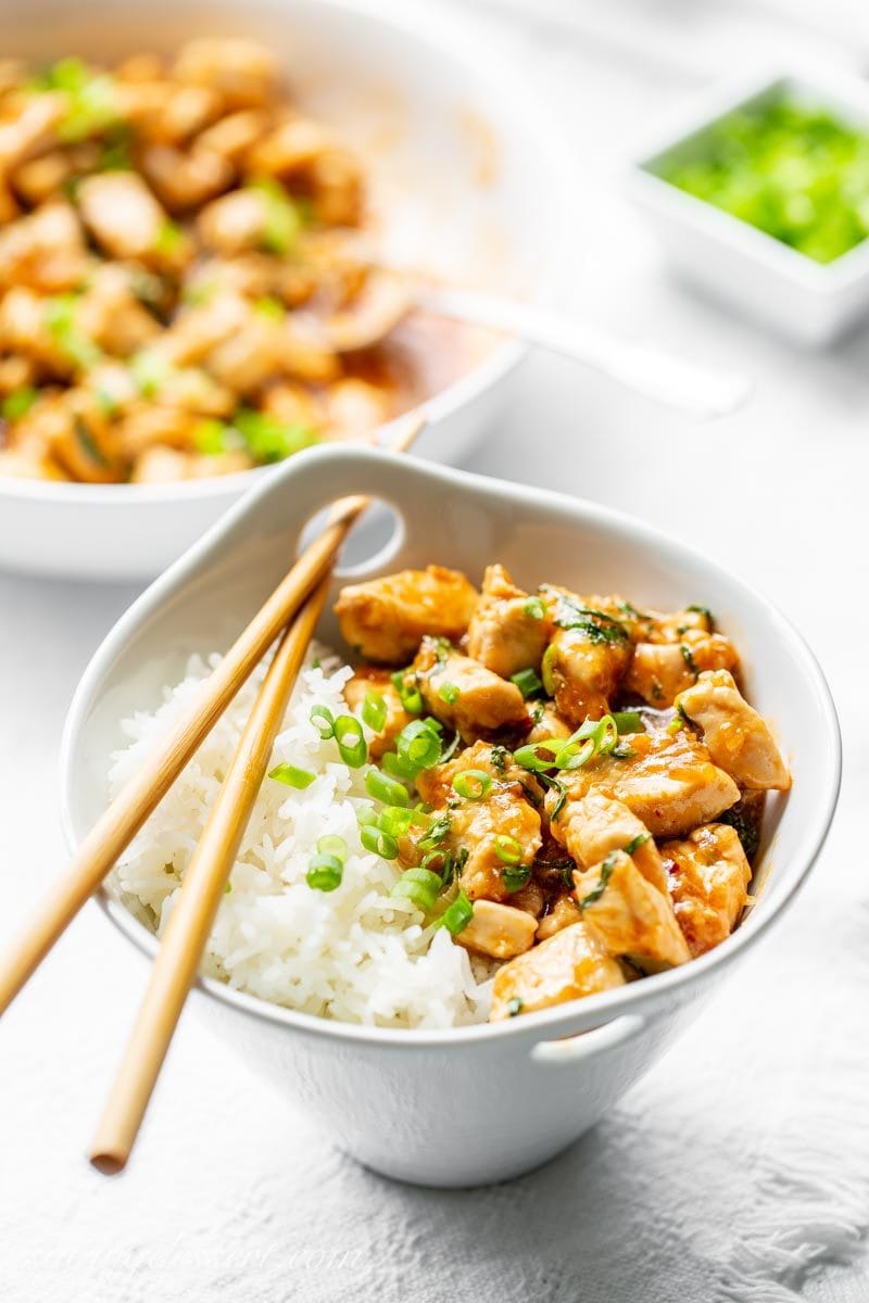 A bowl of Spicy Basil Chicken with Jasmine rice and sliced green onions with chop sticks.