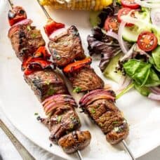 Steak Kabobs on a plate with salad and corn on the cob