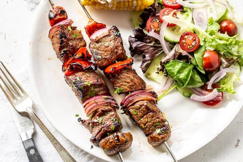 Steak Kabobs on a plate with salad and corn on the cob