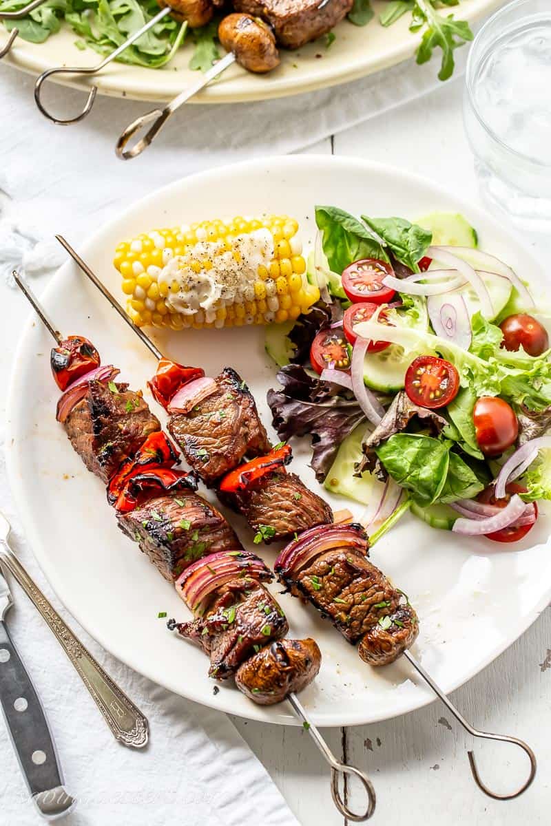 Overhead view of a plate with skewers of grilled steak, salad and corn on the cob