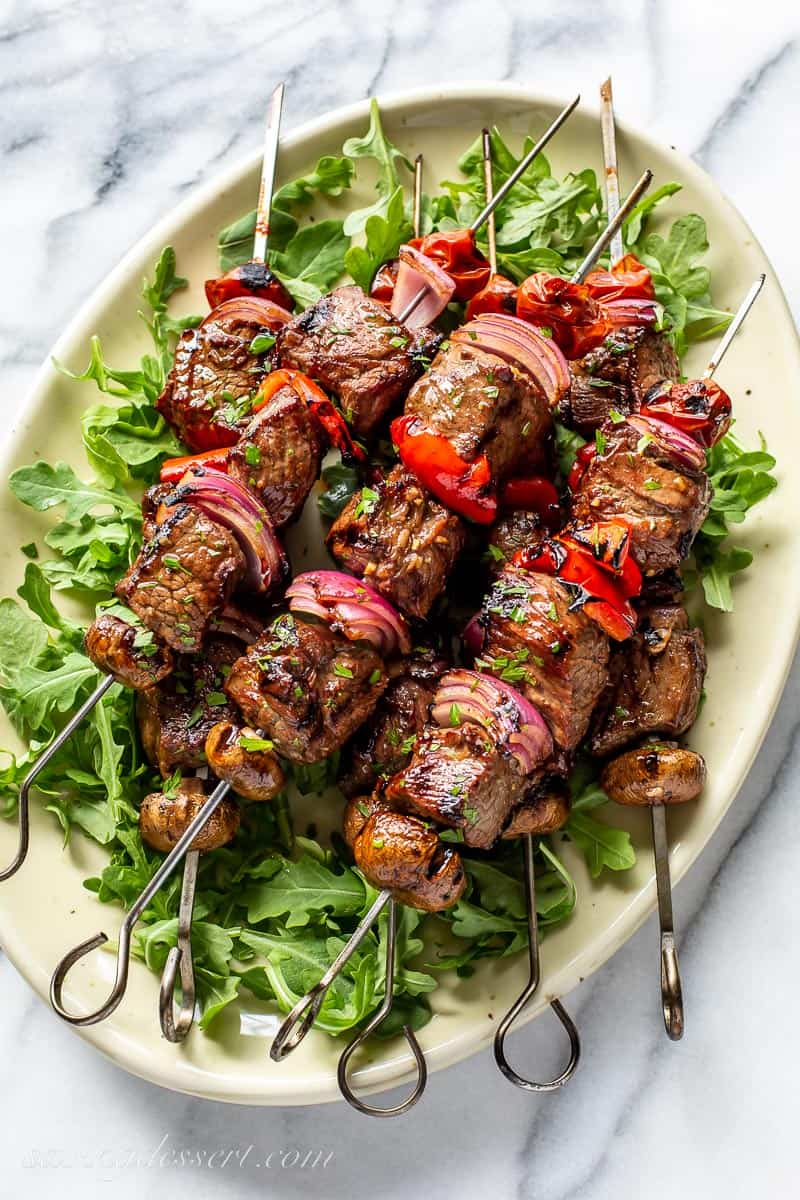 Steak Kabobs on a platter over arugula greens