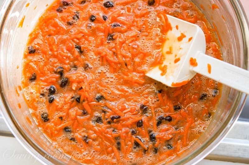 carrot cake batter in a bowl with currants, carrots and a spatula