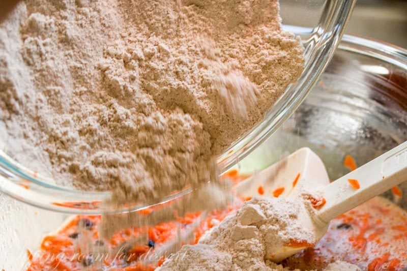 flour mixture for carrot cake being poured into a bowl of carrots and sugar