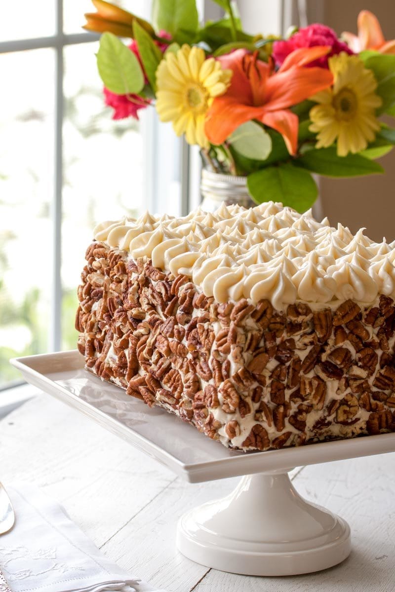 A pecan coated rectangle shaped carrot cake on a cake stand