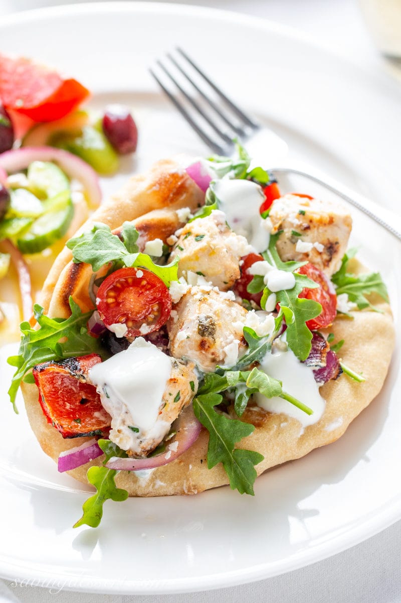 A pita sandwich with grilled chicken, tomatoes, arugula, grilled peppers and onions drizzled with a lemon yogurt sauce