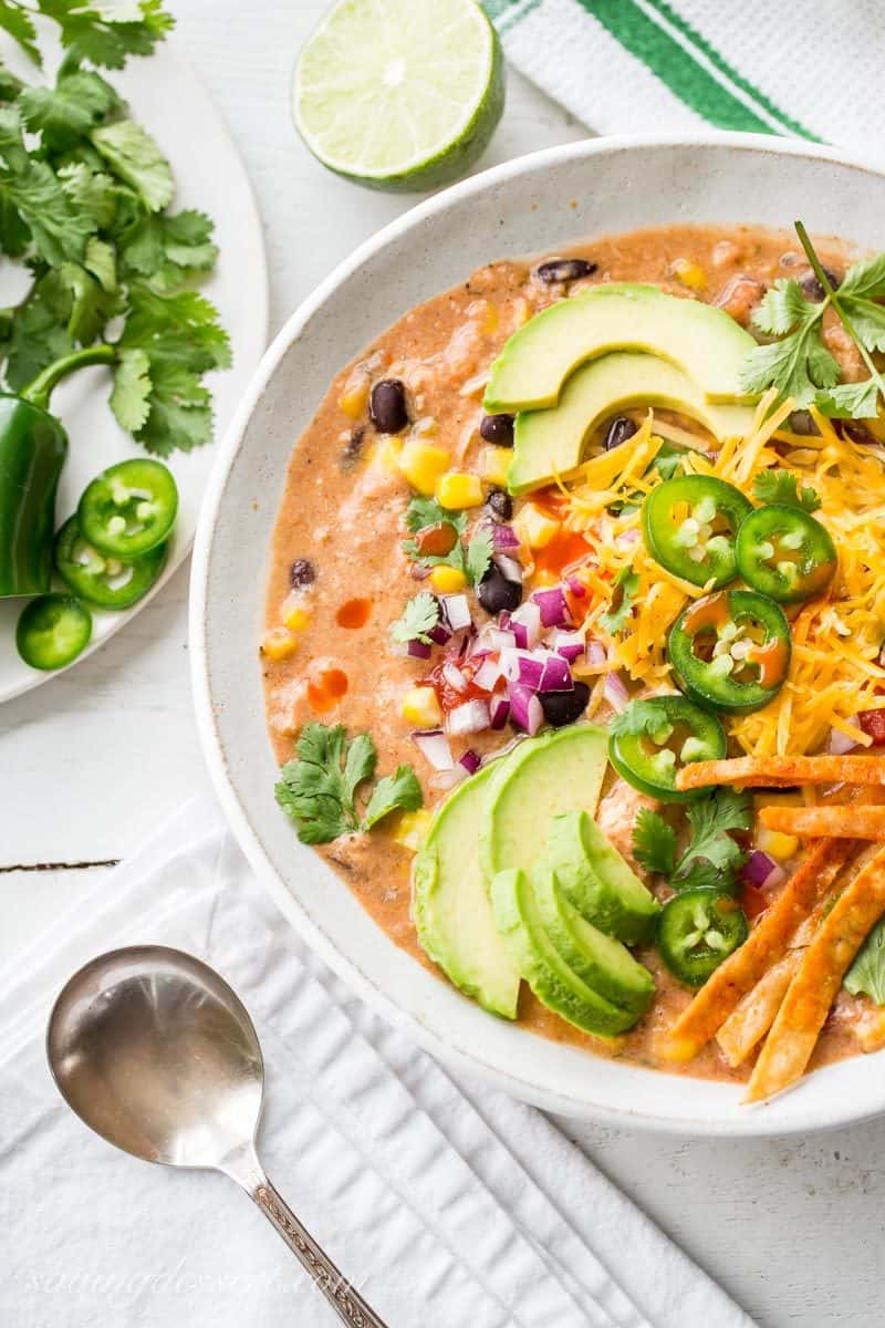 A bowl of creamy taco soup garnished with avocado, cheese, red onion and hot peppers