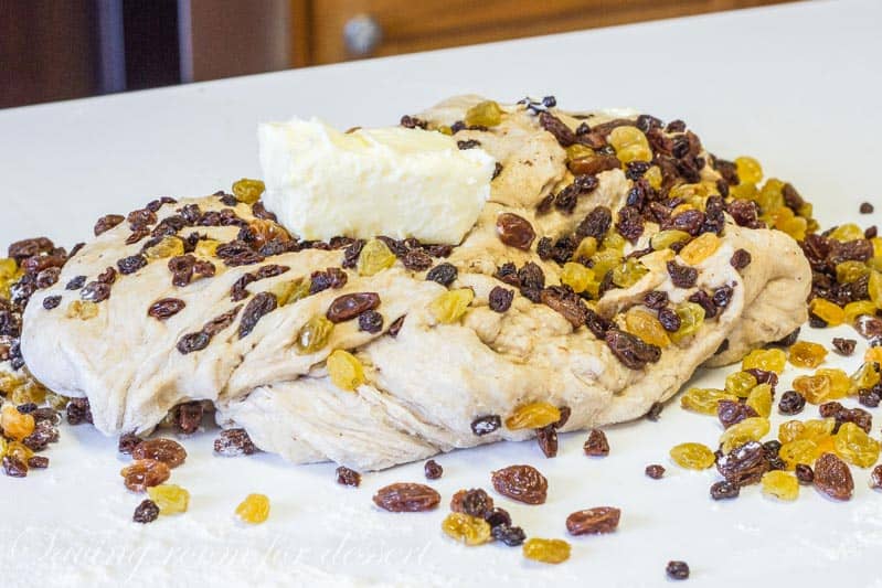 A loaf of bread dough on a counter topped with butter and raisins