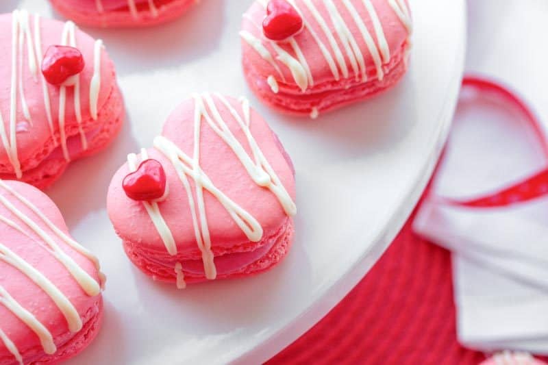 Raspberry Macarons - simple heart shaped macarons using the Italian method, with tips, tricks and how-to instructions for the best cookies. Filled with a fresh raspberry buttercream and topped with a drizzle of white chocolate. Great for Valentine's Day! www.savingdessert.com 