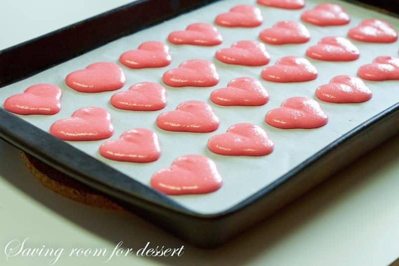 Raspberry Macarons - simple heart shaped macarons using the Italian method, with tips, tricks and how-to instructions for the best cookies. Filled with a fresh raspberry buttercream and topped with a drizzle of white chocolate. Great for Valentine's Day! www.savingdessert.com 