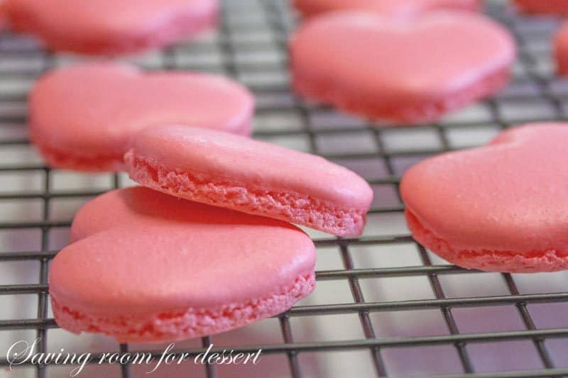 Raspberry Macarons - simple heart shaped macarons using the Italian method, with tips, tricks and how-to instructions for the best cookies. Filled with a fresh raspberry buttercream and topped with a drizzle of white chocolate. Great for Valentine's Day! www.savingdessert.com