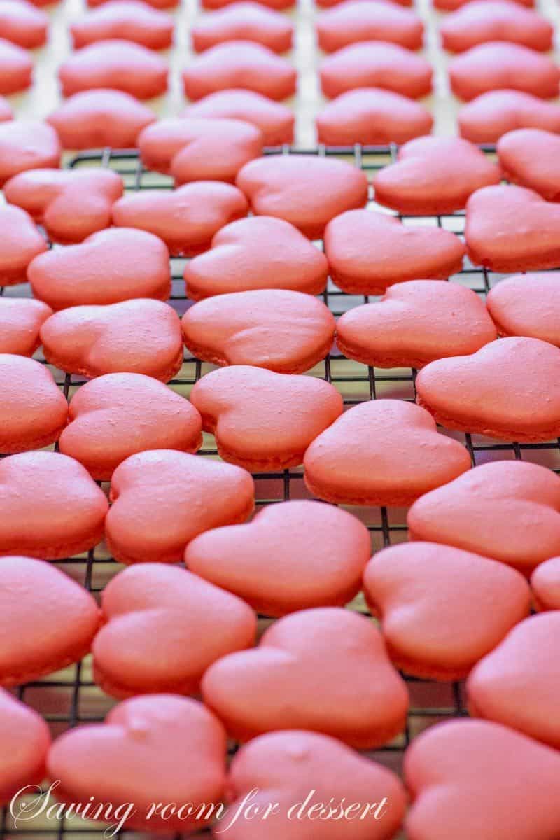 Raspberry Macarons - simple heart shaped macarons using the Italian method, with tips, tricks and how-to instructions for the best cookies. Filled with a fresh raspberry buttercream and topped with a drizzle of white chocolate. Great for Valentine's Day! www.savingdessert.com 