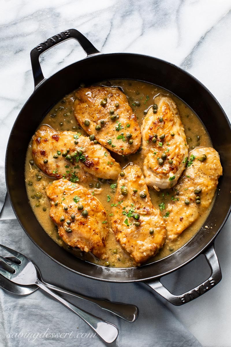 A cast iron skillet filled with chicken cutlets in a lemon sauce with capers