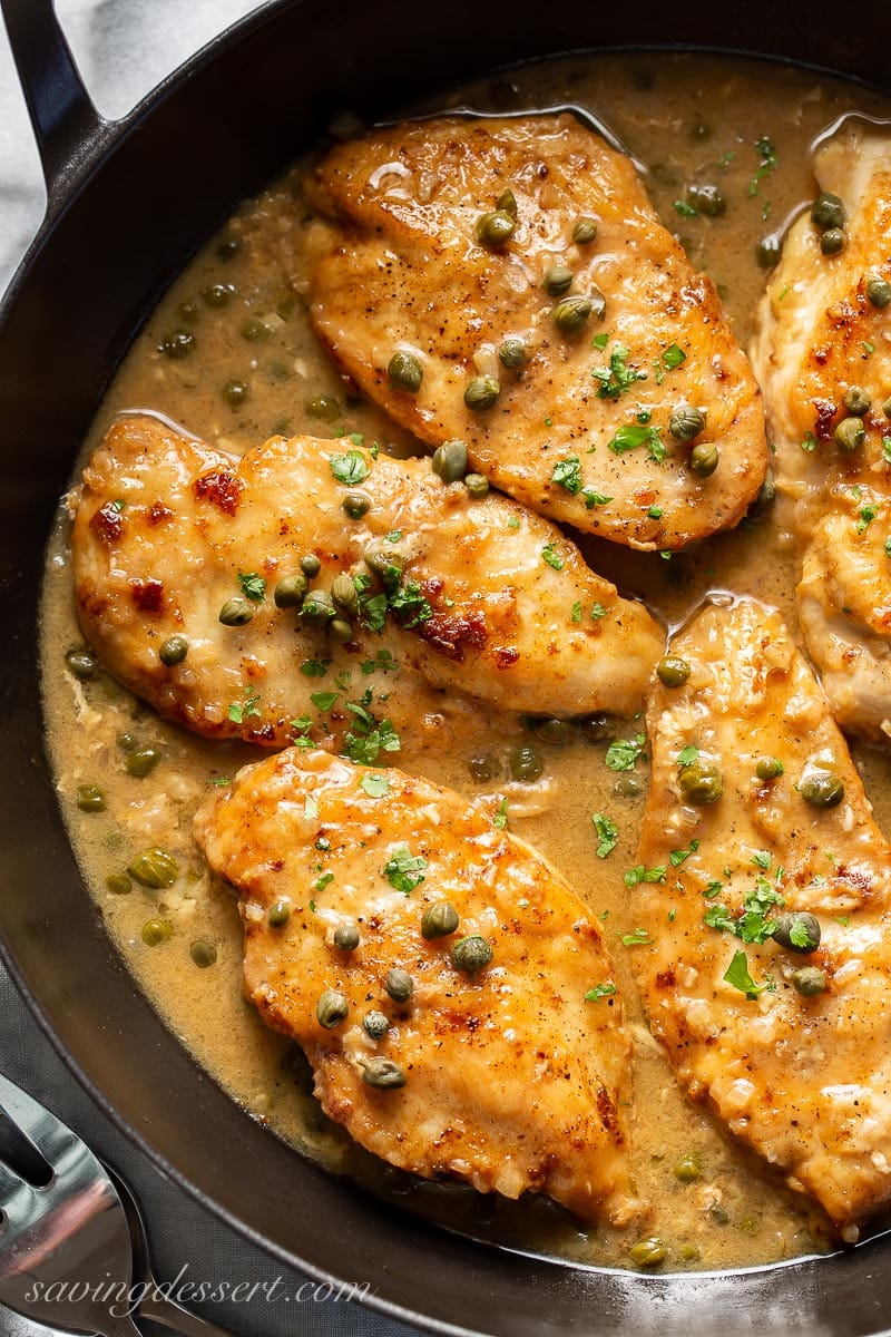 A close up of chicken cutlers in a lemon sauce with capers and parsley