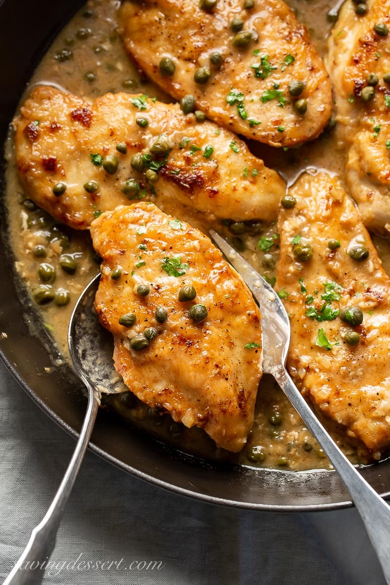 A large serving fork and spoon with a piece of chicken from a skillet