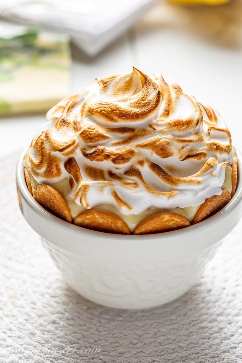 A bowl of meringue topped pudding with vanilla wafers on the side