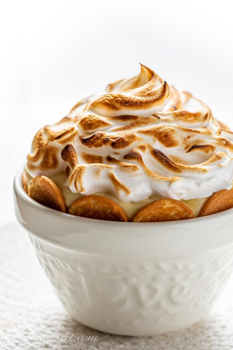 A side view of a white bowl filled with pudding and vanilla wafers topped with a toasted meringue