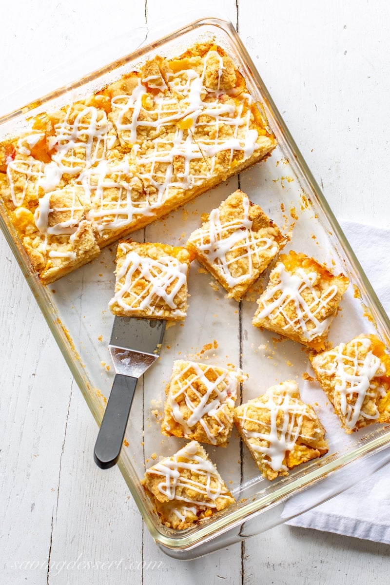 A baking pan with fresh peach crumb bars topped with a drizzle of icing