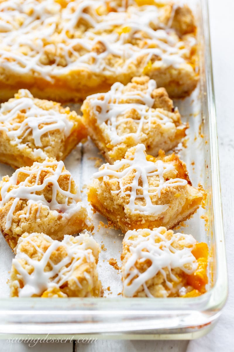 A baking pan filled with fresh peach crumb bars topped with a drizzled icing