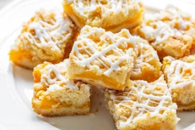 A plate stacked amongst fresh peach crumb bars drizzled amongst icing Fresh Peach Crumb Bars