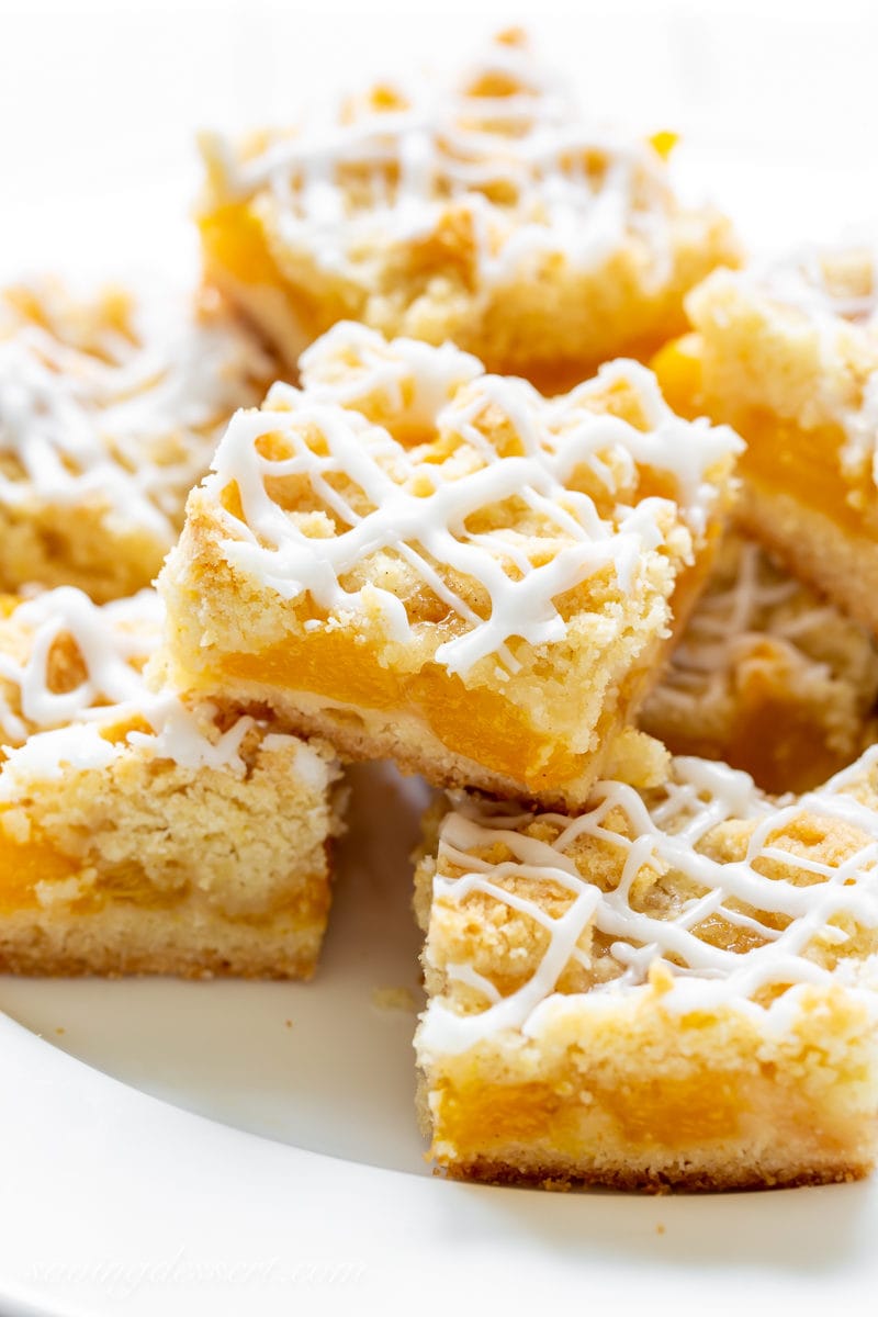 A plate stacked with fresh peach crumb bars drizzled with icing