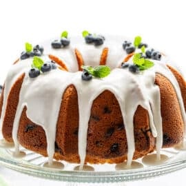 A side view of a blueberry pound cake topped with white lemon icing and fresh blueberries.