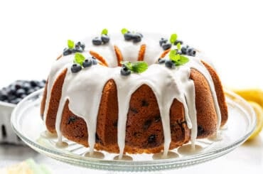 A side view of a blueberry pound cake topped with white lemon icing and fresh blueberries.