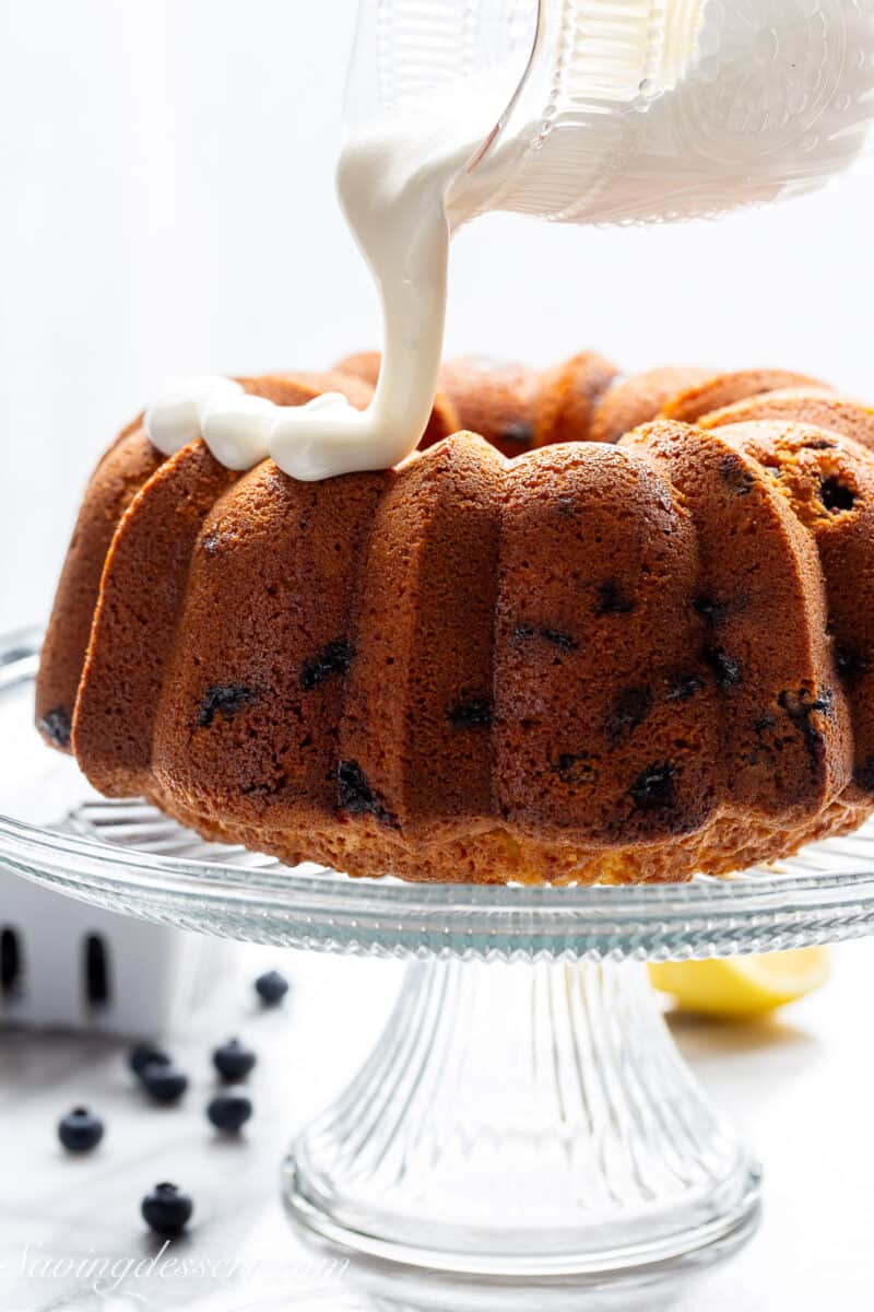 A blueberry pound cake being drizzled with thick white lemon icing.