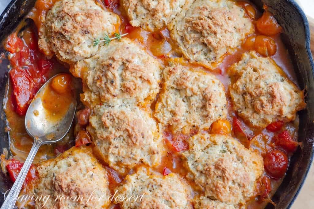 A closeup of a tomato cobbler topped with herbed biscuits.