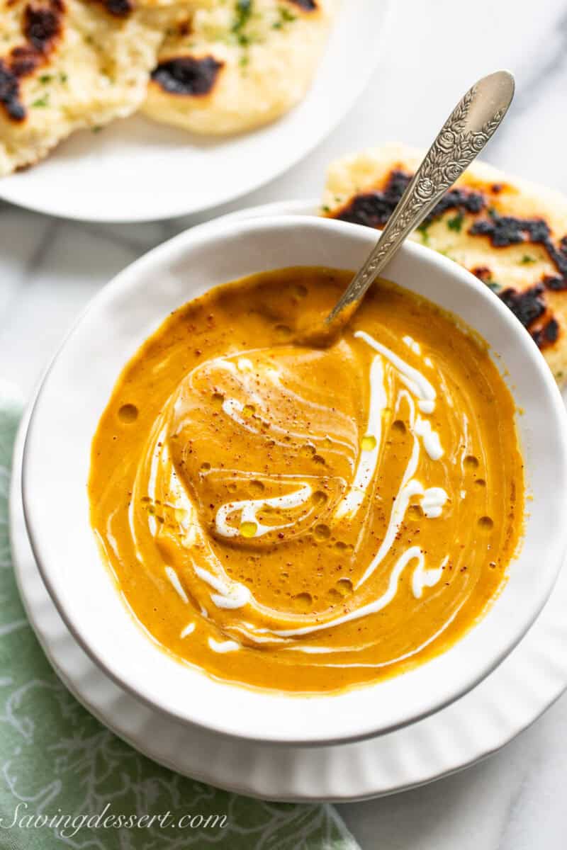 An overhead of a bowl of golden butternut squash soup served with naan bread on the side.