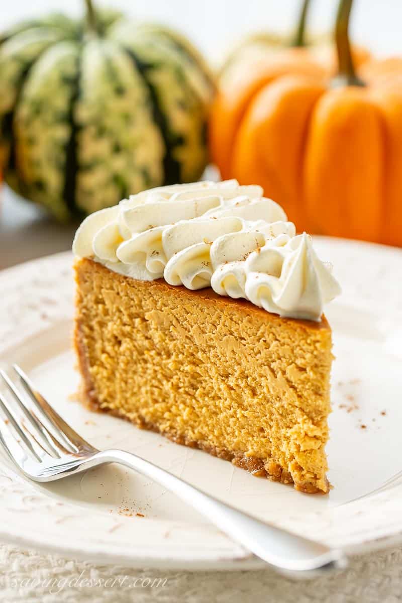 Closeup of a slice of pumpkin cheesecake topped with loads of whipped cream swirls