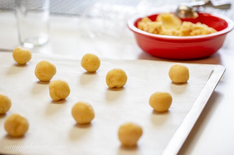 A red bowl of cookie dough with dough balls on a baking sheet lined with parchment paper