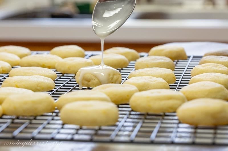 Lemon meltaway cookies on a cooling rack being drizzled with lemon icing