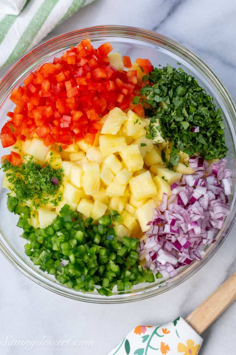 A large mixing bowl filled with chopped peppers, pineapple, cilantro and onion.