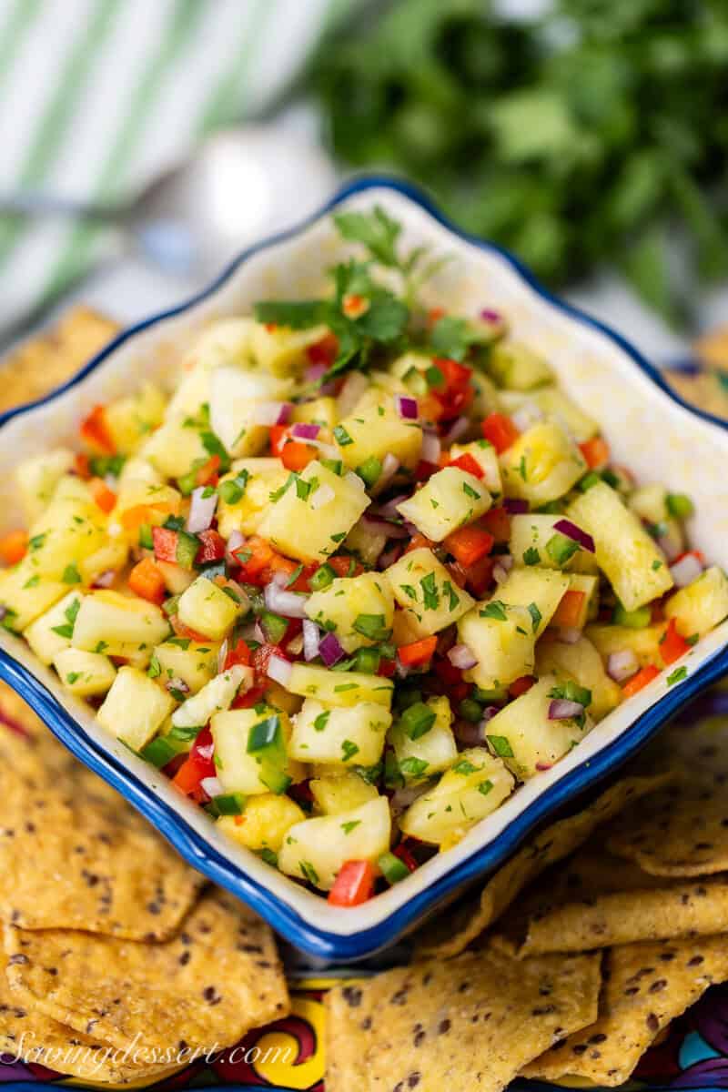 Pineapple salsa in a colorful blue bowl with chips and cilantro on the side.