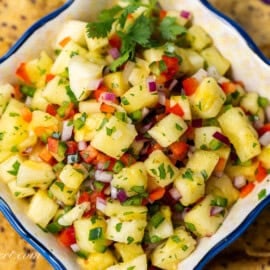 A closeup photo of a bowl of pineapple salsa with chips scattered around the bowl.