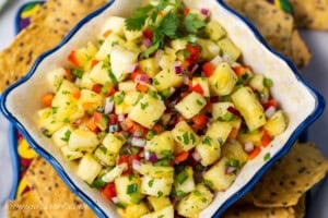 A closeup photo of a bowl of pineapple salsa with chips scattered around the bowl.