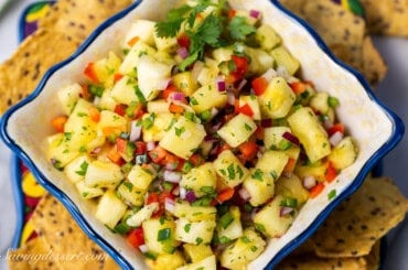 A closeup photo of a bowl of pineapple salsa with chips scattered around the bowl.