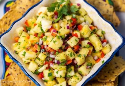 A closeup photo of a bowl of pineapple salsa with chips scattered around the bowl.