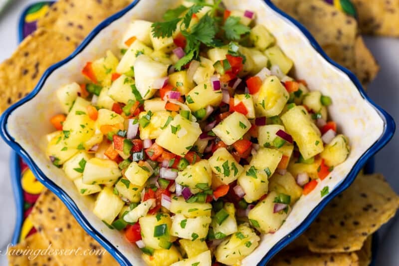 A closeup photo of a bowl of pineapple salsa with chips scattered around the bowl.