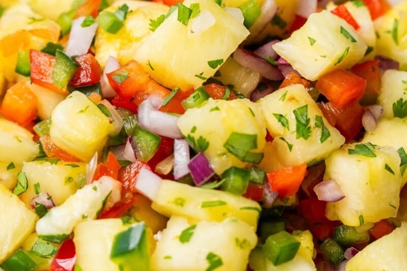 An overhead view of a bowl of pineapple salsa with cilantro and jalapeño peppers.