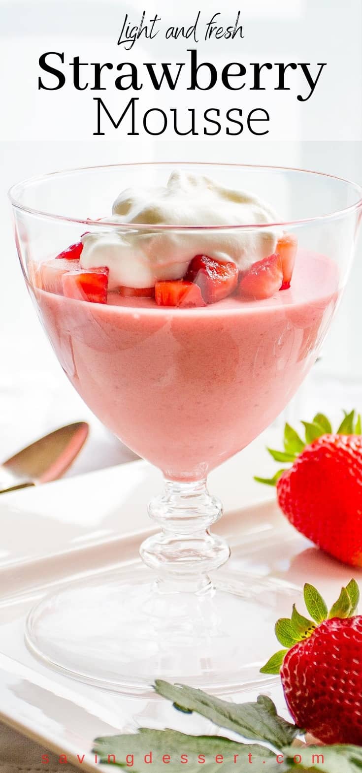 A stemmed serving glass filled with strawberry mousse topped with diced strawberries and whipped cream
