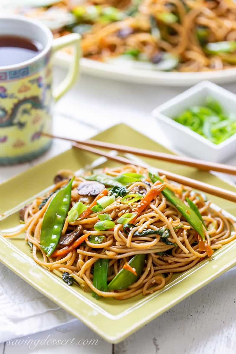 A plate of lo mein with vegetables and chop skicks