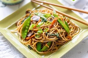 Close up of a plate of vegetable lo mein with chop sticks