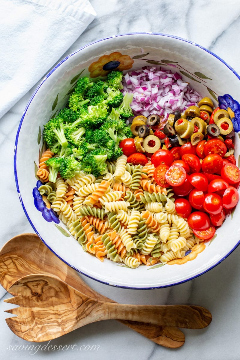 An overhead view of a big bowl of pasta noddles with broccoli, red onion, olives and tomatoes